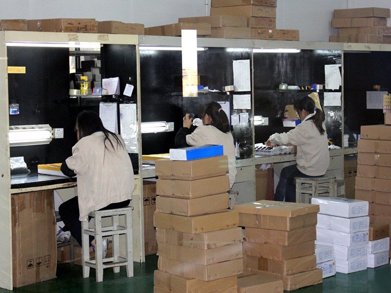 Lens inspection benches with boxes of lenses. Photograph from the Jiayu factory pages.