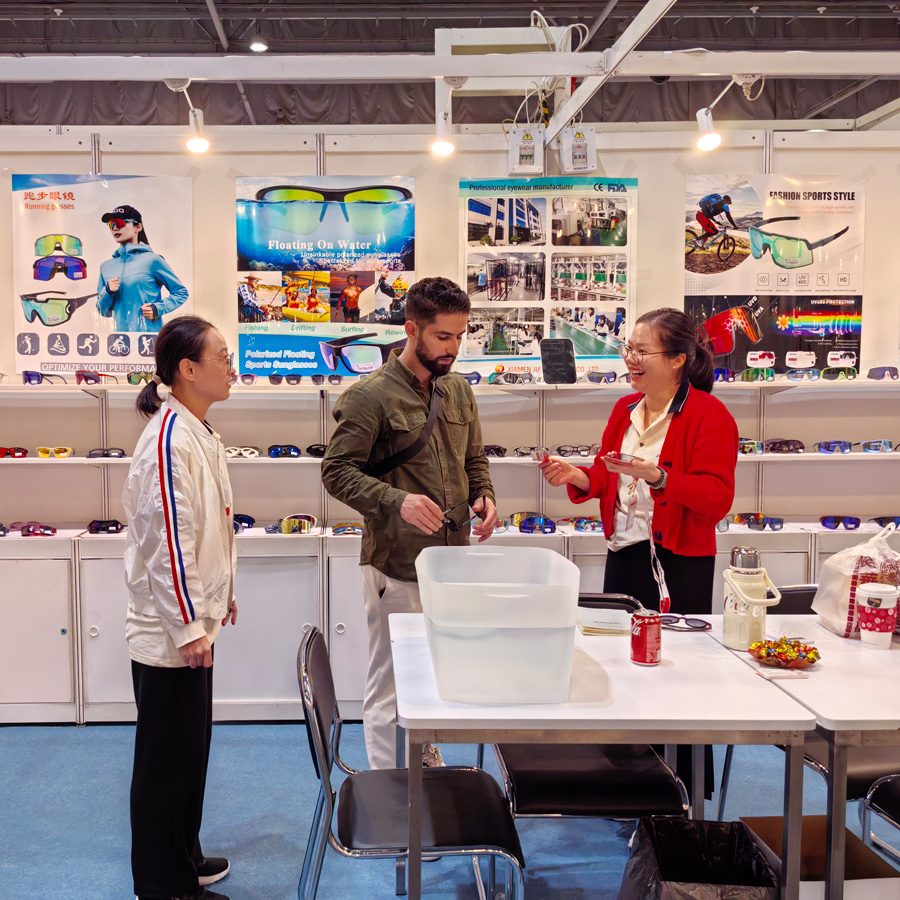 Visitors at a Jiayu fair booth with sunglasses posters and a water tray on the table